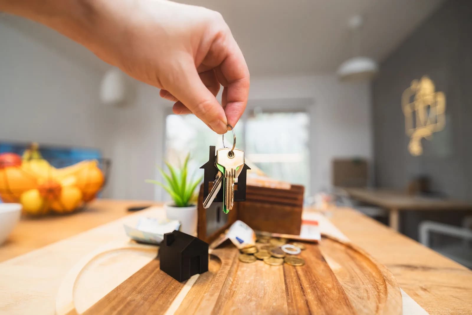 A hand holding a new house-shaped keychain, with a kitchen table in the background