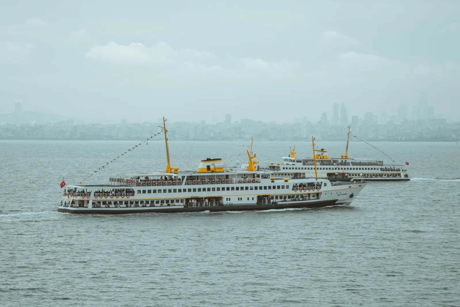 Two passenger ferries crossing the sea in front of the Istanbul skyline
